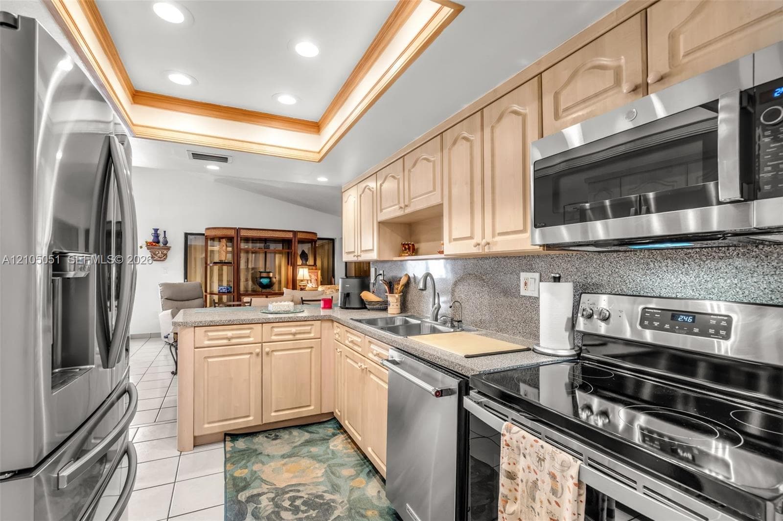 Kitchen featuring light wood cabinetry, stone countertops, stainless steel appliances, and a recessed tray ceiling with integrated lighting