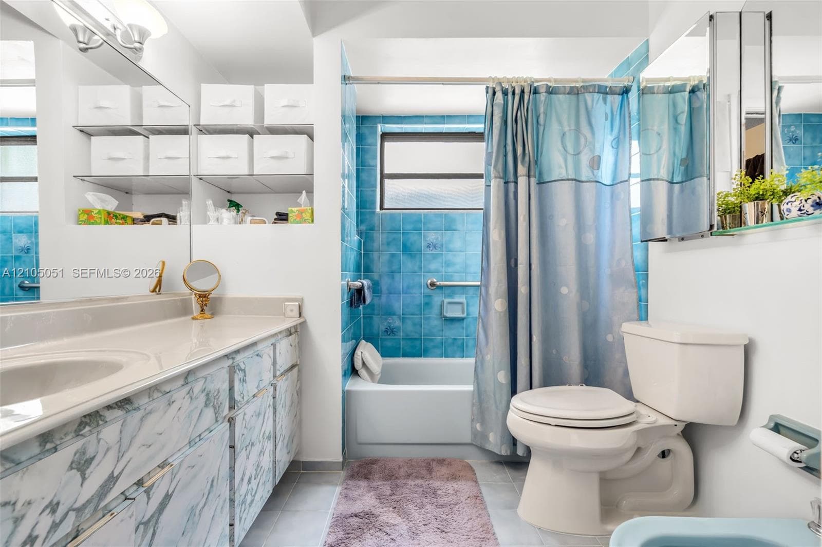 Bathroom featuring a vanity with integrated sink and stone-patterned cabinetry, blue tile tub surround, inset shelving, and a wall-mounted mirrored medicine cabinet