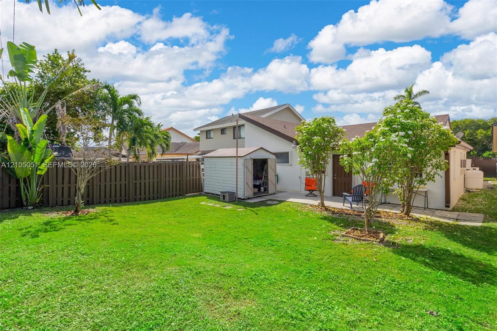 Backyard featuring a manicured lawn, perimeter wood privacy fencing, a concrete patio, and mature landscaping