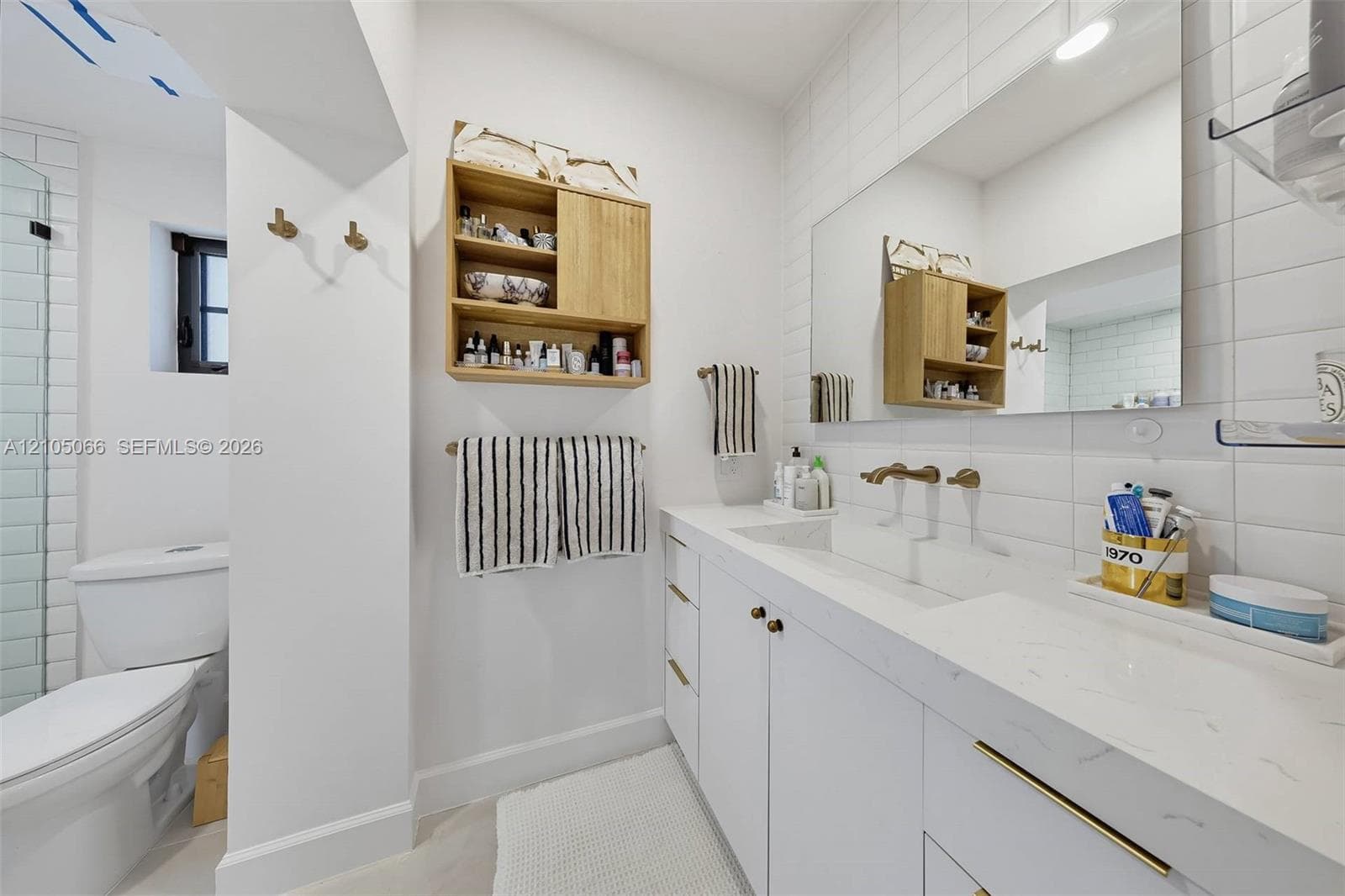 Bathroom featuring a white vanity with integrated double sinks, quartz countertop, brass-tone hardware, wall-mounted faucets, and subway tile wall surrounds