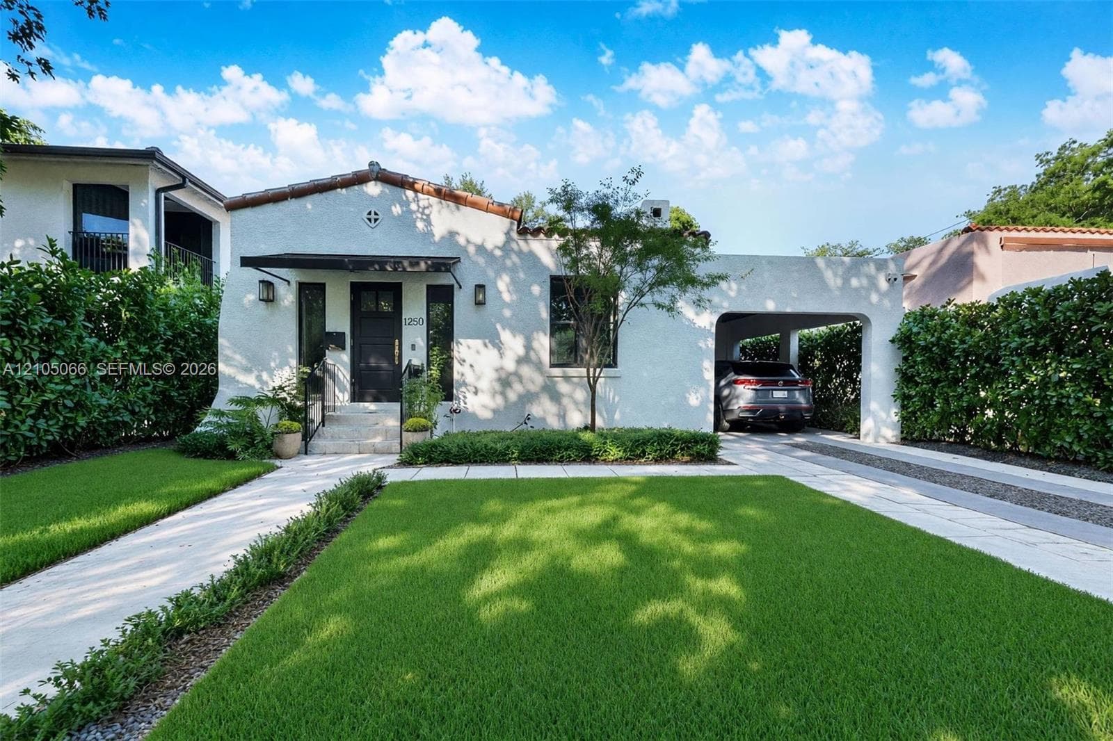Stucco exterior featuring a clay tile roof, arched carport, private walkway, and mature landscaping