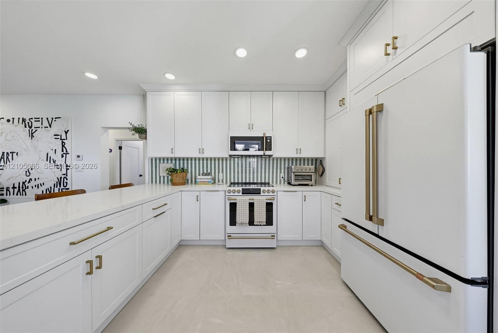 Kitchen featuring white shaker-style cabinetry, quartz countertops, a green and white vertical tile backsplash, gold-toned hardware, and white-finish appliances