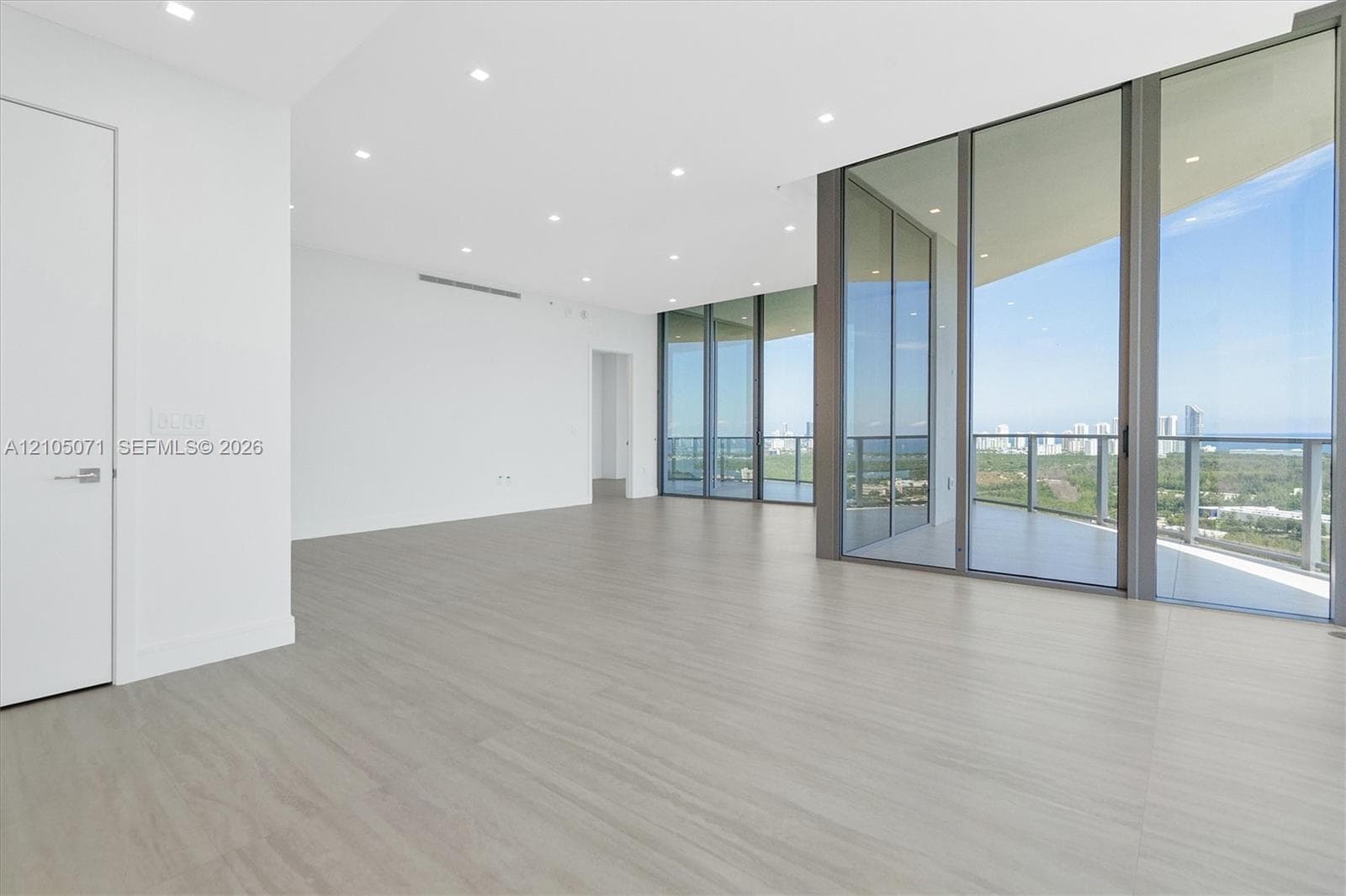 Open living area featuring wood-finish flooring, floor-to-ceiling glass walls, recessed lighting, and a wrap-around balcony with metal railing