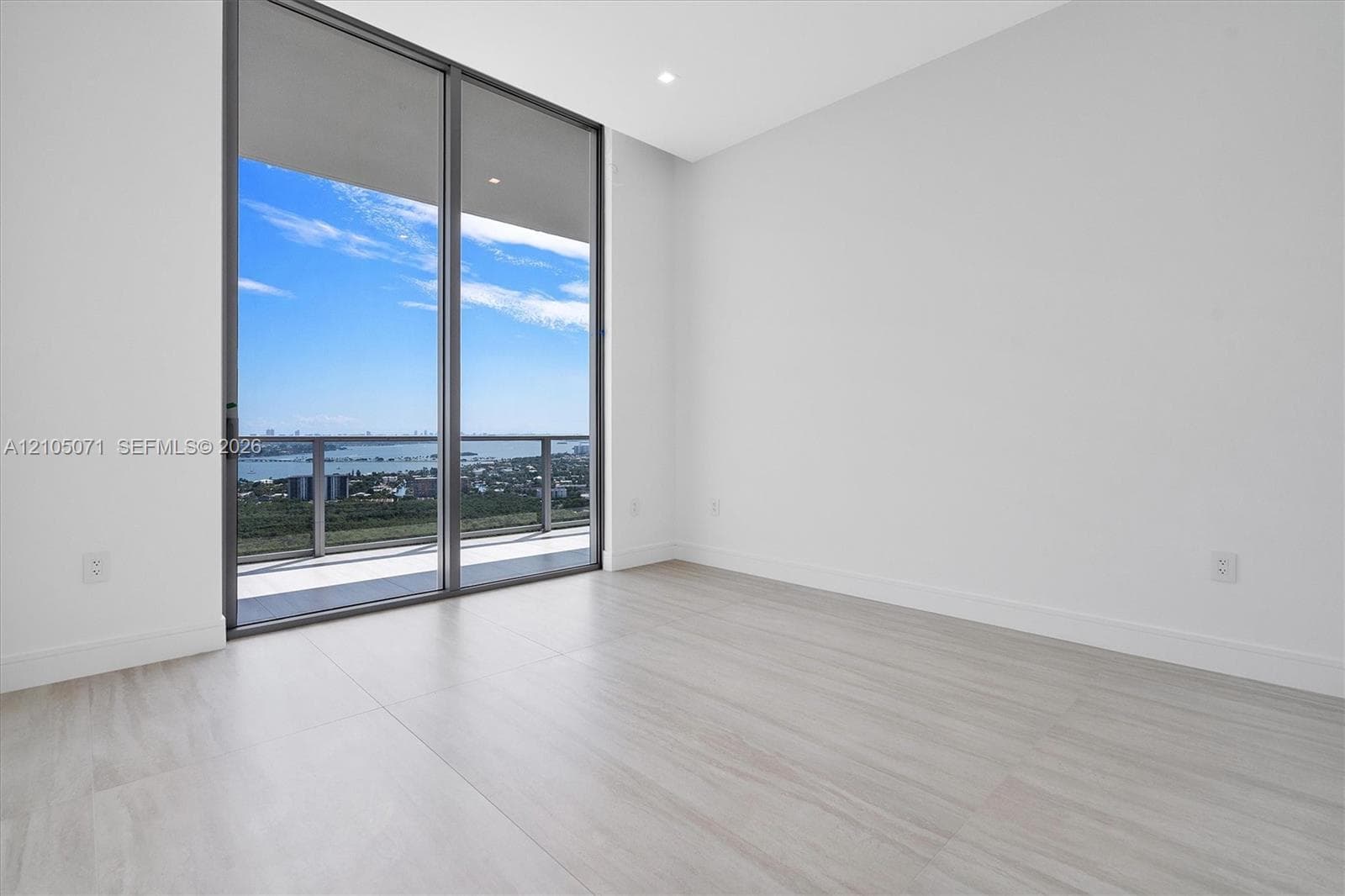 Floor-to-ceiling sliding glass doors, neutral wood-finish flooring, recessed lighting, and a balcony with metal railing