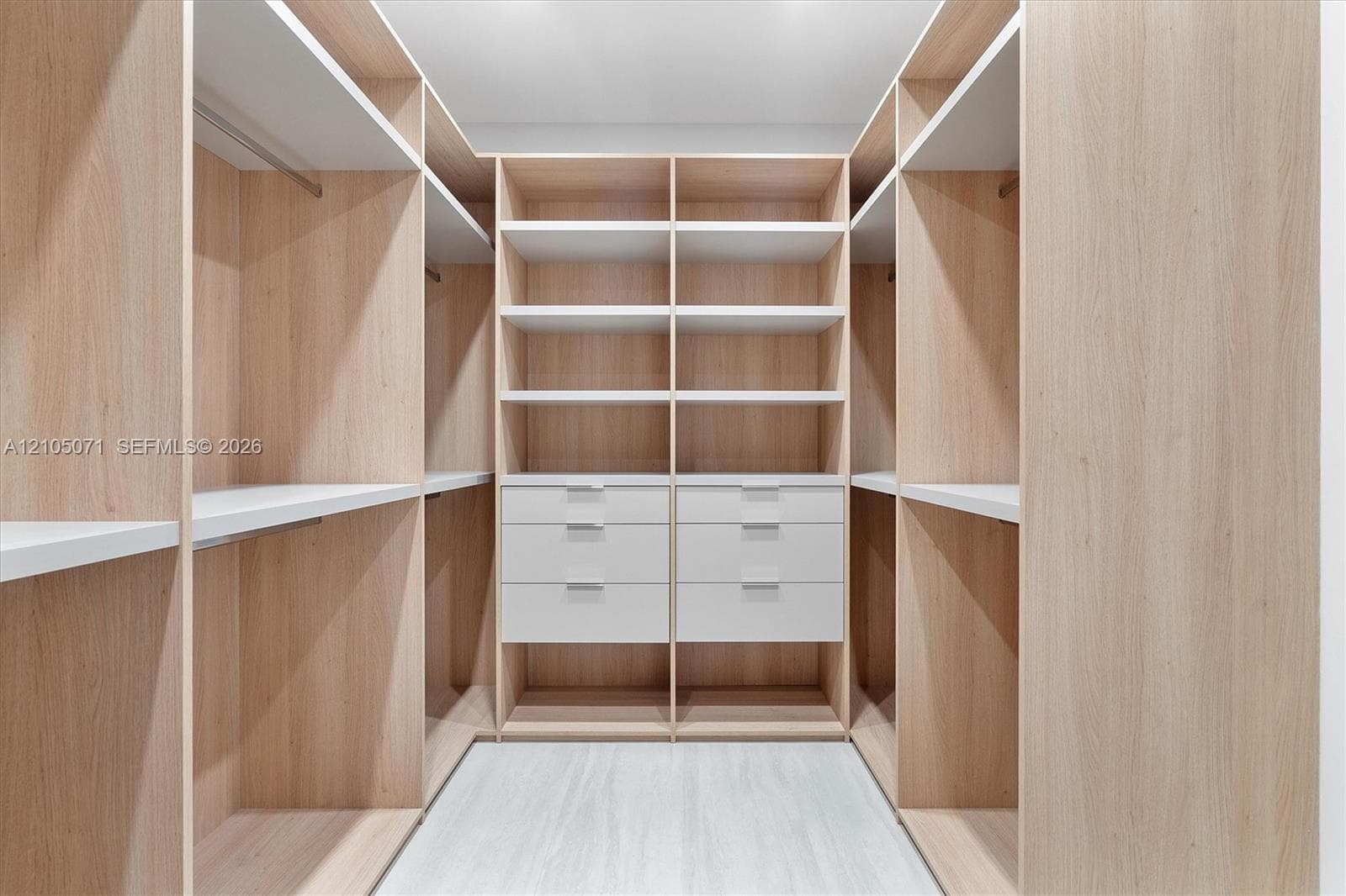 Walk-in closet featuring custom wood-finish built-in cabinetry, multiple open shelving tiers, integrated clothing rods, and white flat-panel drawers