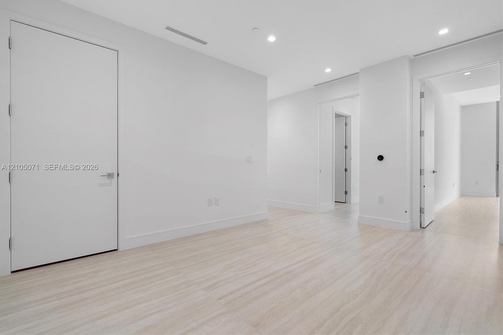 Neutral interior featuring light wood-finish flooring, recessed ceiling lighting, and solid-core doors with brushed-metal hardware