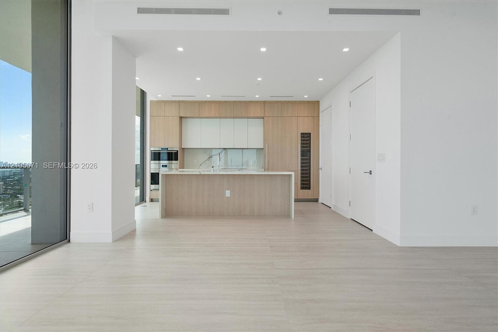 Modern kitchen featuring light wood-finish cabinetry, a central island, recessed ceiling lighting, and floor-to-ceiling glass sliding doors