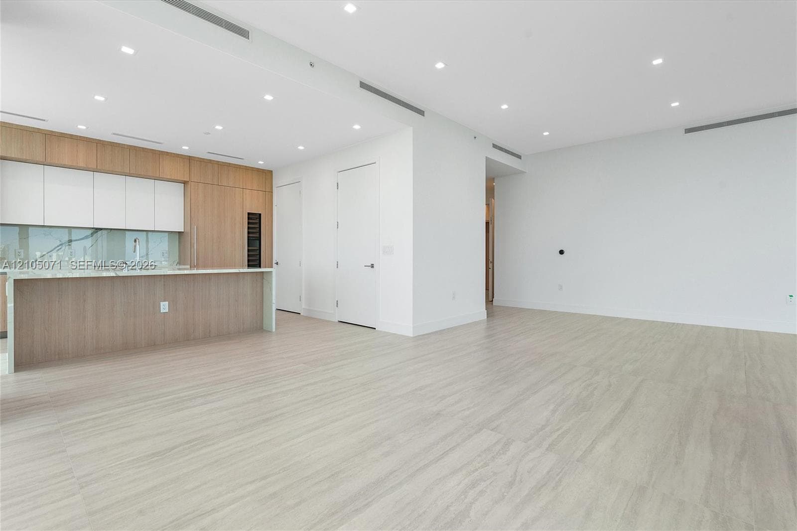 Open-concept living space featuring wood-finish flooring, recessed lighting, integrated cabinetry, stone-surface island, and built-in wine storage