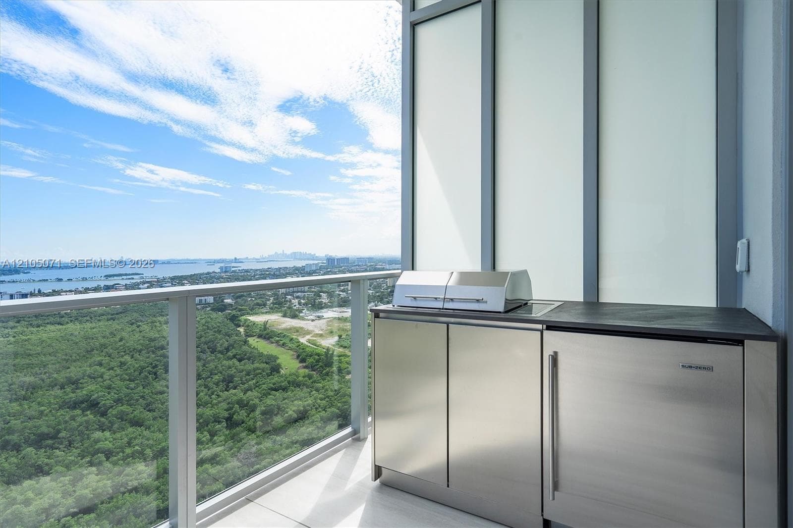 Private balcony featuring a stainless steel outdoor kitchen, built-in grill, integrated under-counter refrigeration, and glass panel railing overlooking the horizon