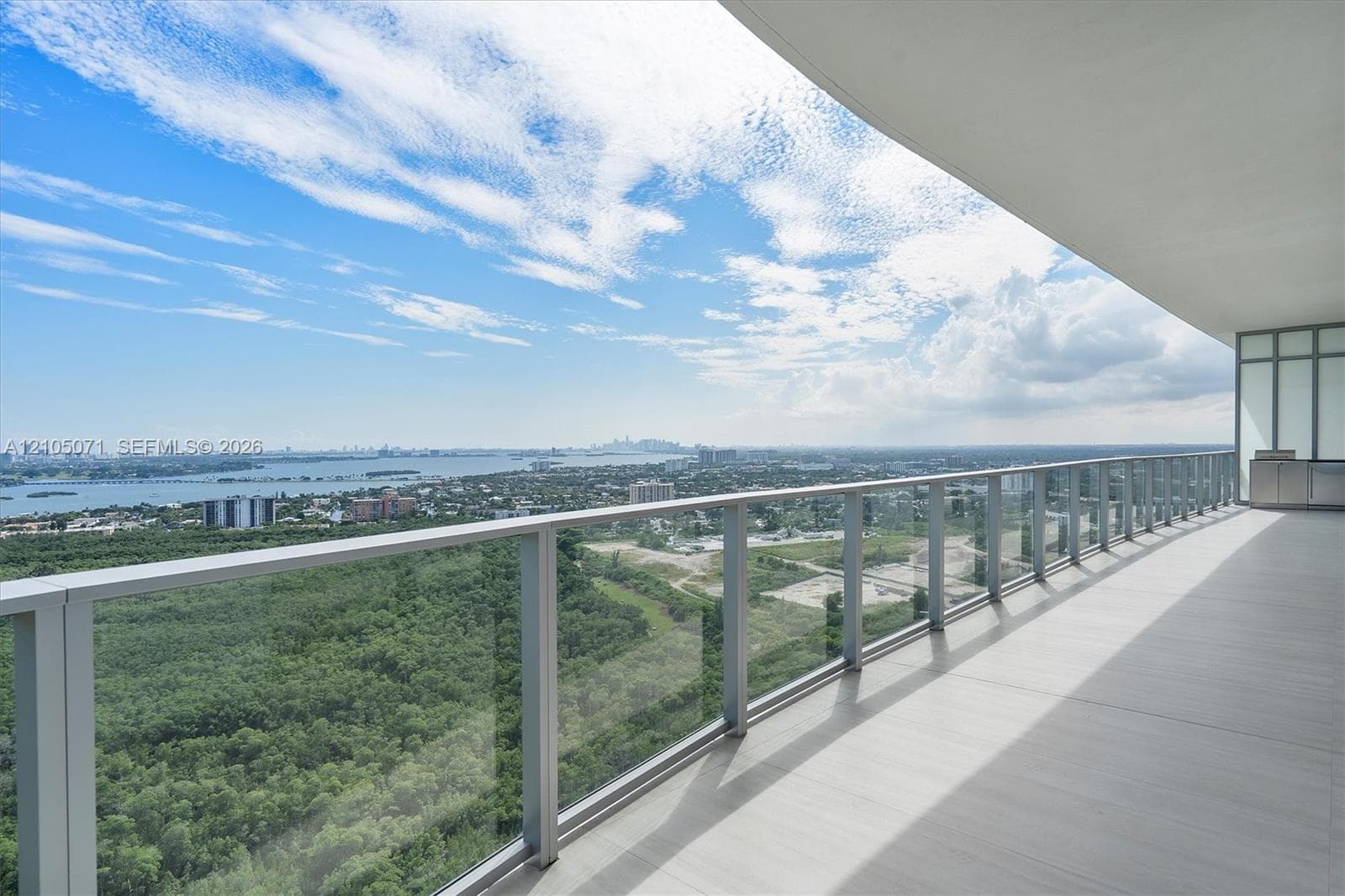 Expansive covered balcony featuring large-format tile flooring and a sleek glass-panel railing