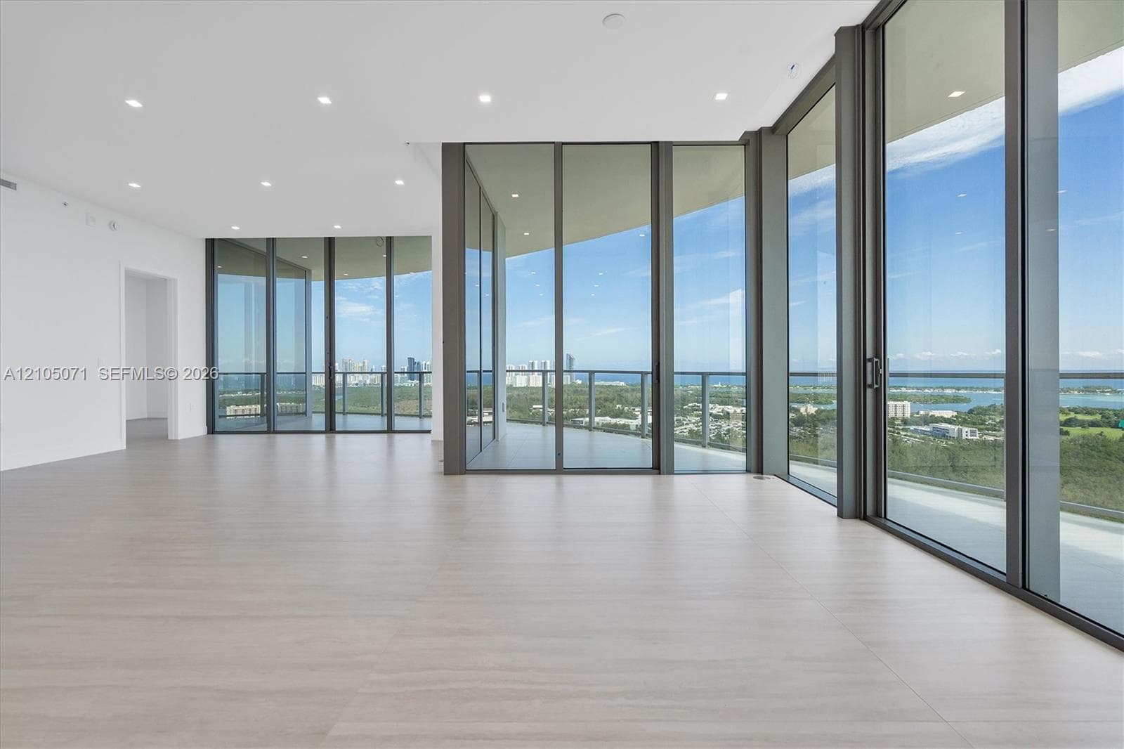Floor-to-ceiling glass walls, expansive wraparound balcony with a metal railing, light-toned tile flooring, and recessed ceiling lighting