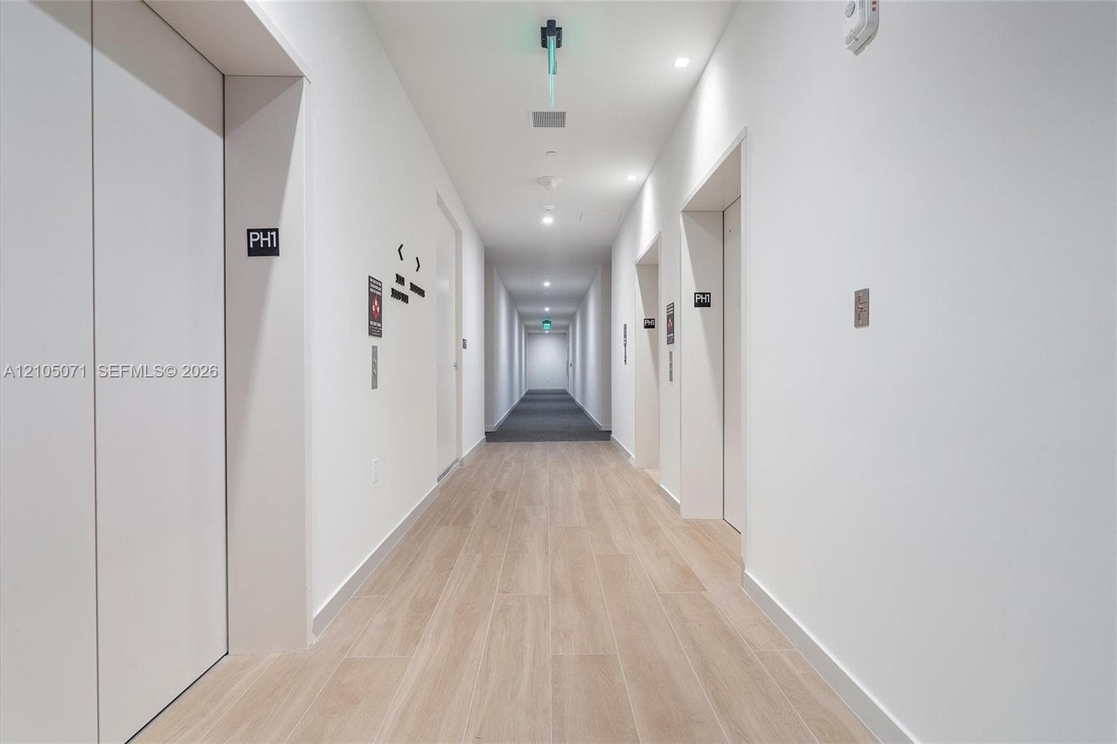 Hallway featuring wood-finish flooring, recessed ceiling lighting, and smooth white walls