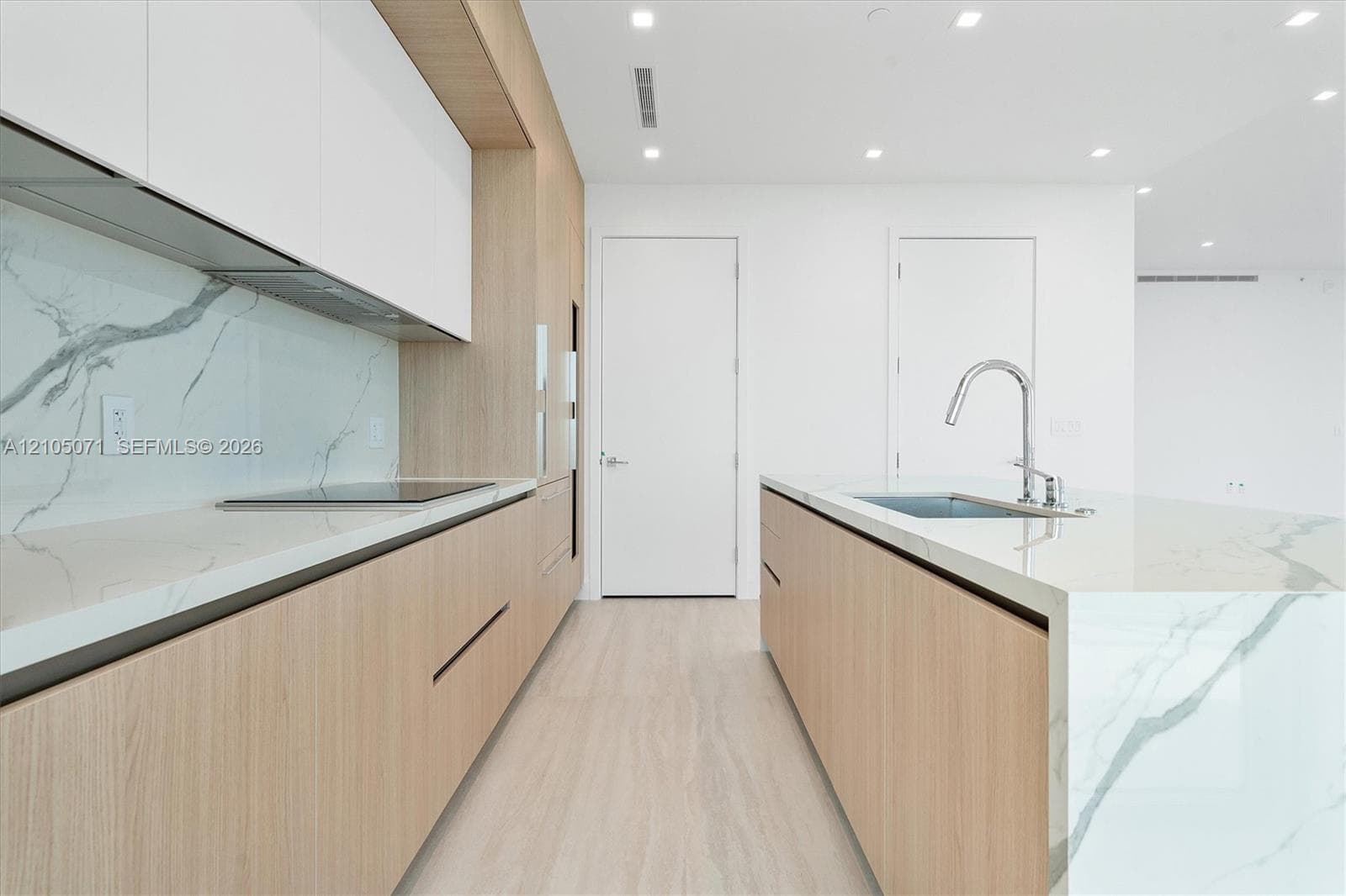 Modern kitchen featuring light wood-finish cabinetry, waterfall-edge stone countertops, full-height stone backsplash, recessed lighting, and a gooseneck faucet