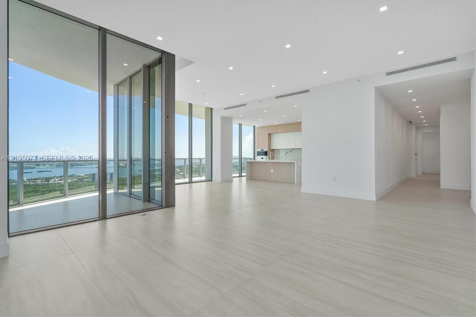 Floor-to-ceiling glass walls, expansive balcony, large-format tile flooring, recessed lighting, and kitchen with integrated cabinetry