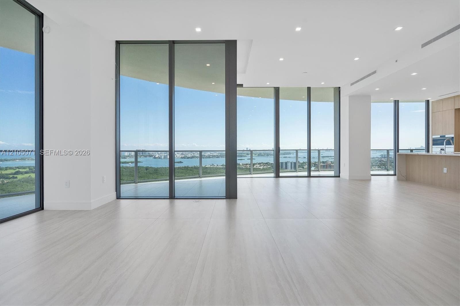 Open-concept interior featuring floor-to-ceiling glass walls, expansive balcony, light-toned wood-finish flooring, and recessed ceiling lighting