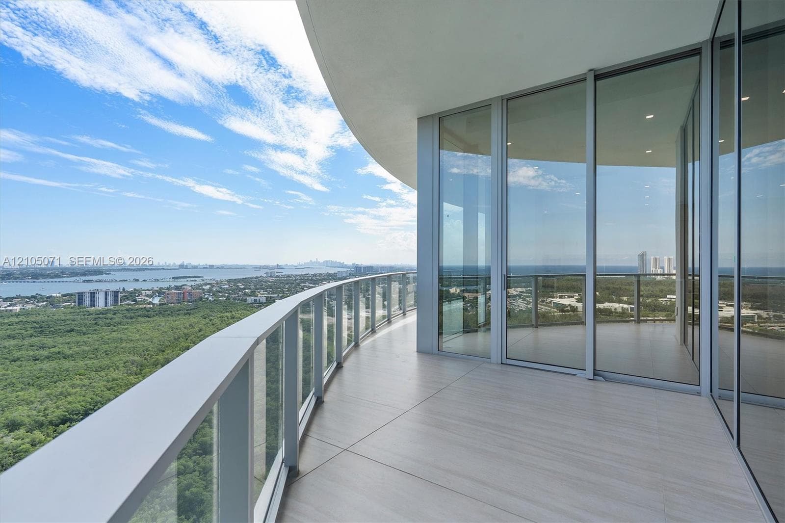 Curved wrap-around balcony featuring large-format tile flooring, a glass-panel railing system, and floor-to-ceiling glass sliding doors