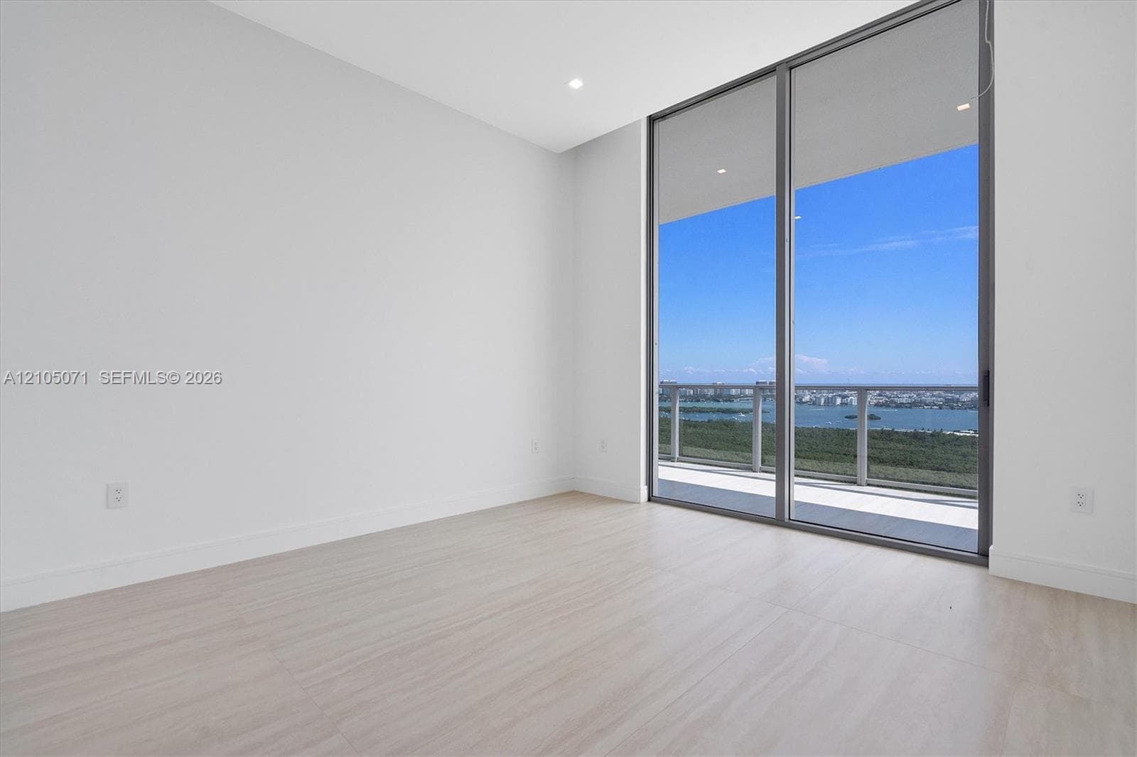 Floor-to-ceiling glass sliding doors, wood-finish flooring, recessed lighting, and a private balcony with water and skyline scenery