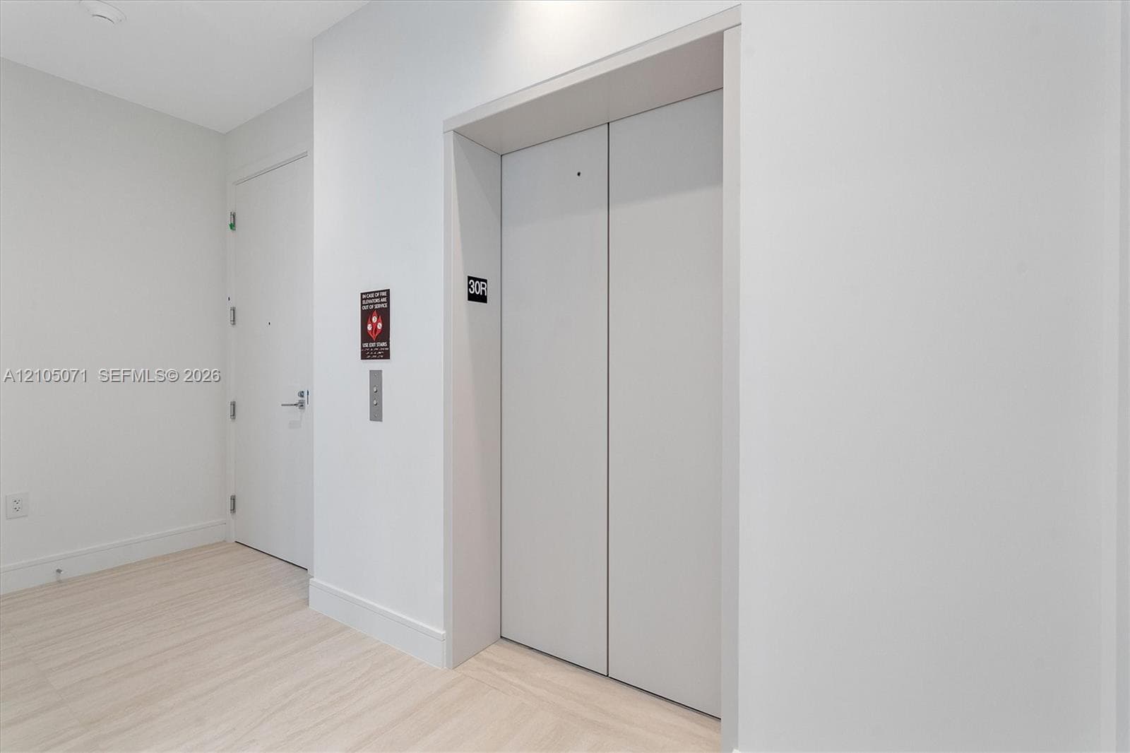 Elevator access with dual metallic doors, light-toned wood-finish flooring, and crisp white wall finishes