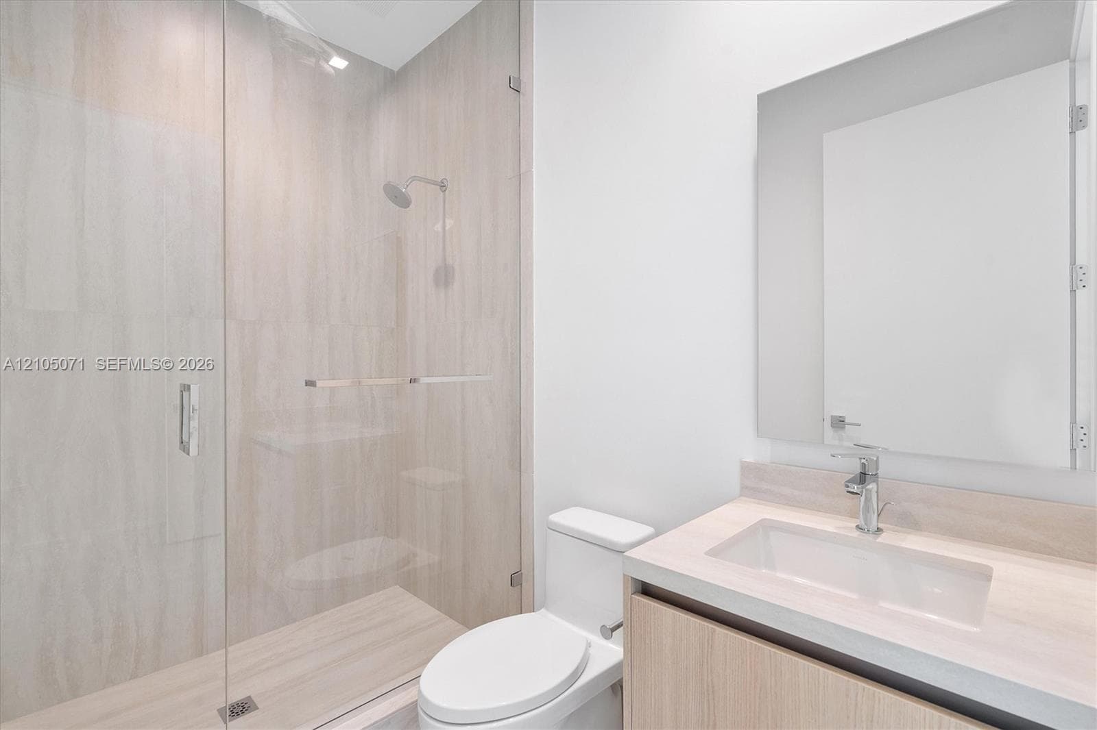 Walk-in shower with floor-to-ceiling tile, glass enclosure, floating wood-finish vanity, integrated rectangular sink, and polished chrome fixtures