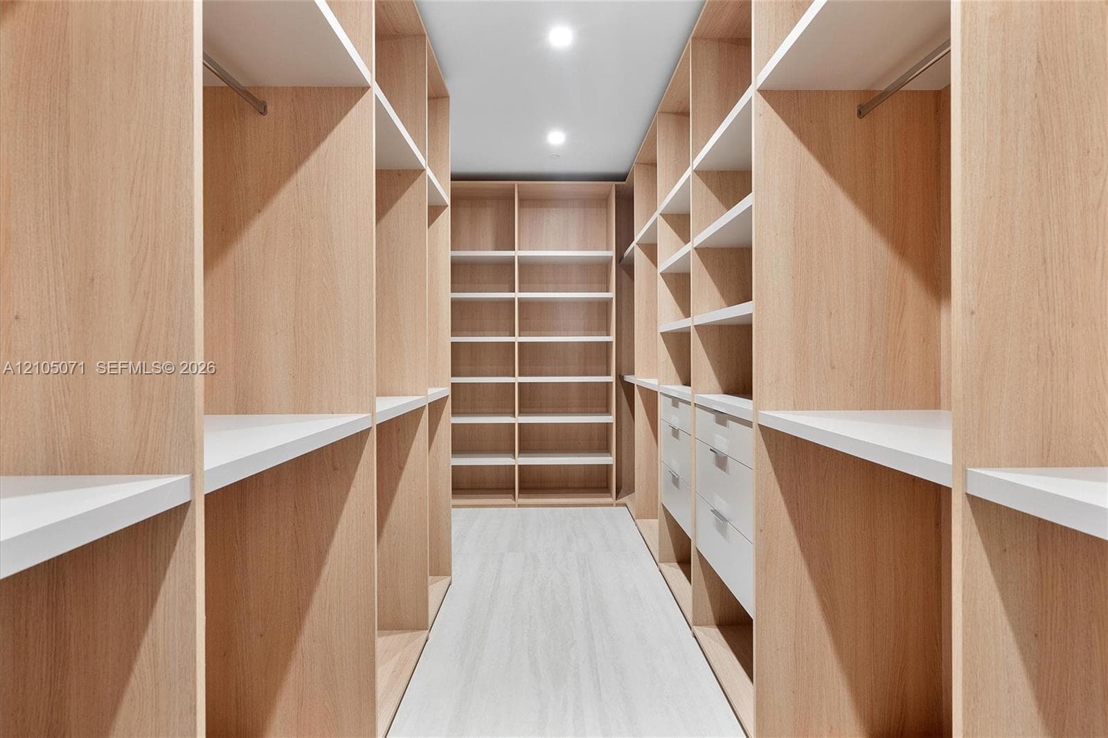 Walk-in closet featuring custom wood-finish built-in cabinetry, multiple adjustable shelving tiers, integrated clothing rods, and recessed lighting