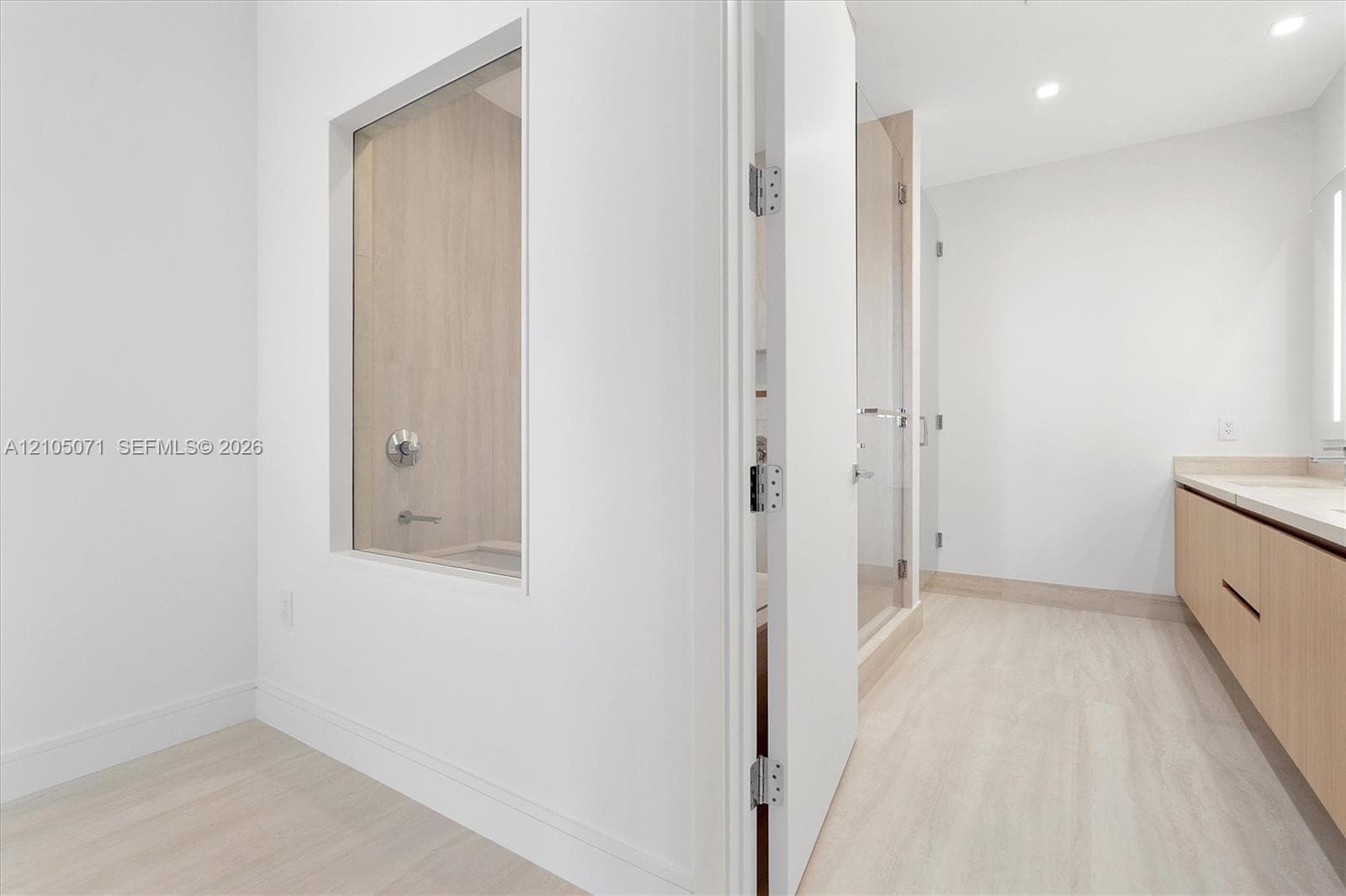 Bathroom featuring a floating vanity with wood-finish cabinetry, a glass-enclosed shower, light wood-finish flooring, and a recessed wall niche