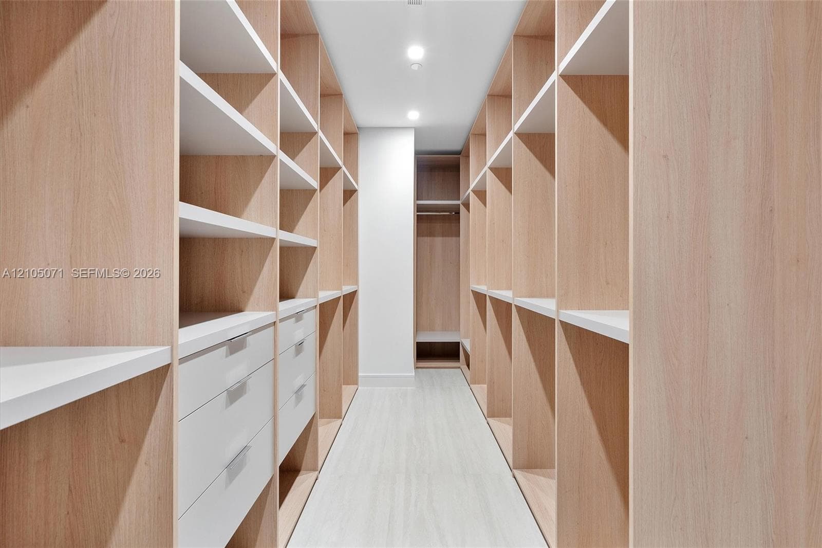 Custom built-in storage featuring light wood-finish shelving, integrated white drawers with metallic hardware, and recessed ceiling lighting