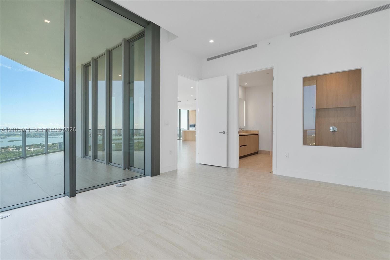 Floor-to-ceiling glass paneling, expansive covered balcony, light wood-finish flooring, recessed lighting, and integrated wall-mounted wood cabinetry