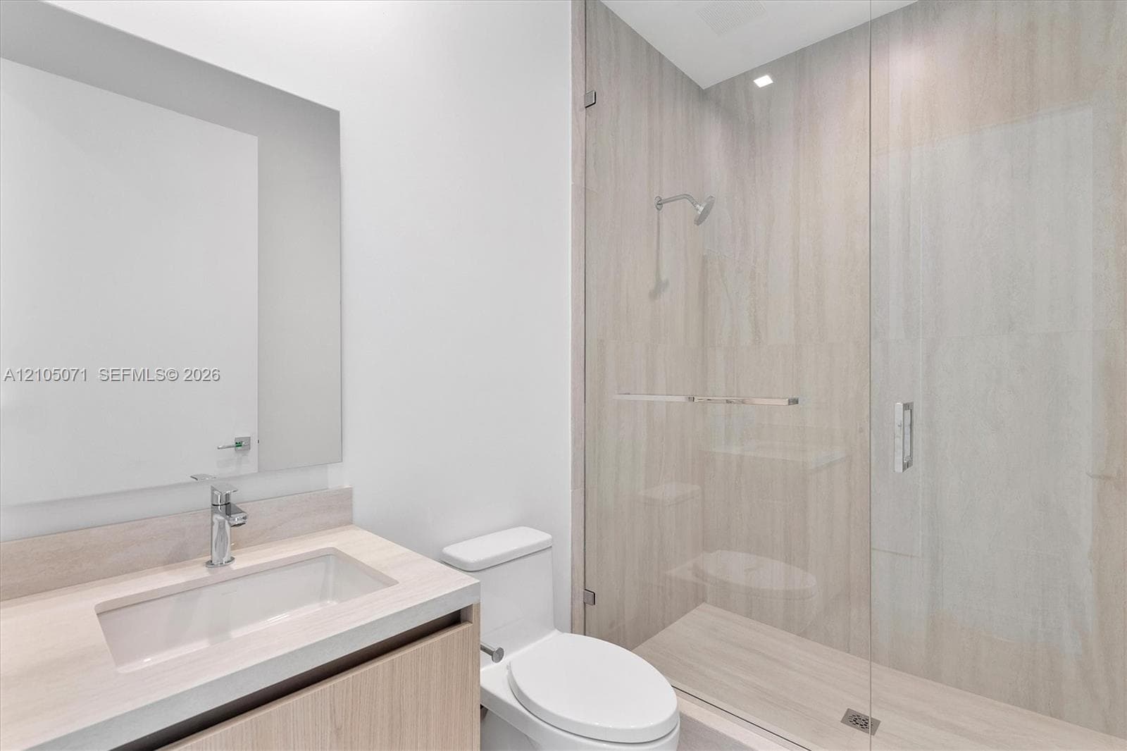 Modern vanity with integrated sink, stone-finish countertop, frameless glass shower enclosure, and full-height stone-finish tile surround