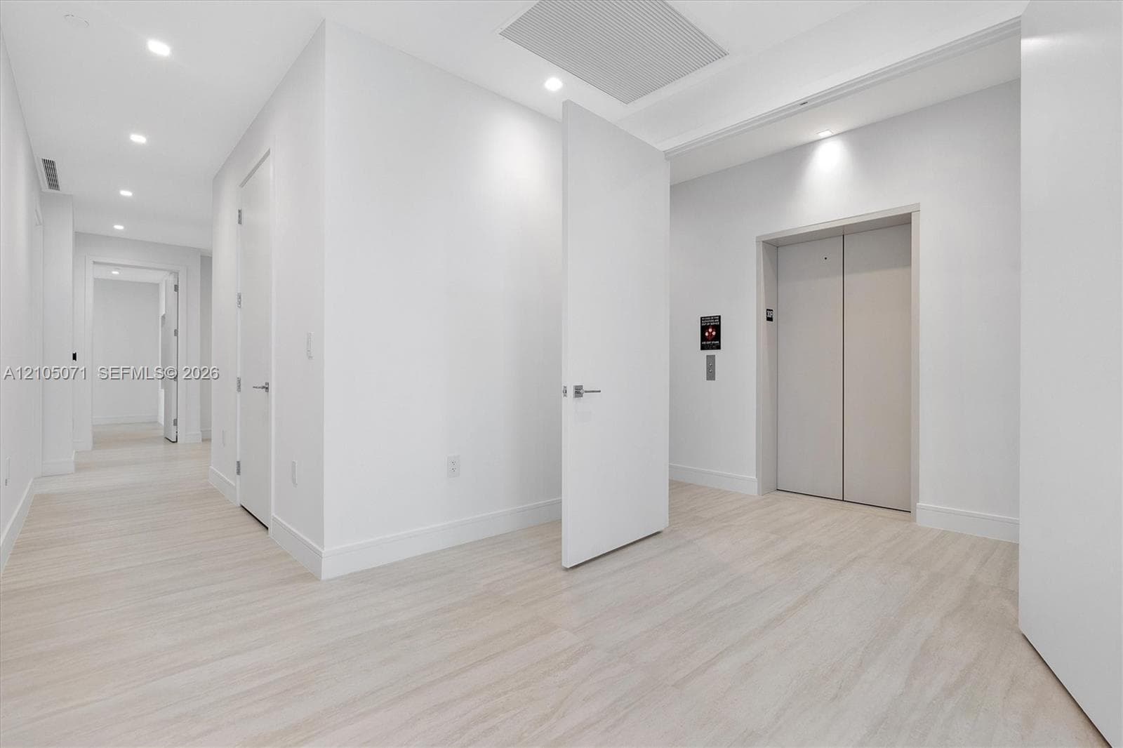 Minimalist interior featuring light wood-finish flooring, recessed ceiling lighting, private elevator access, and flush-mounted interior doors with satin nickel hardware