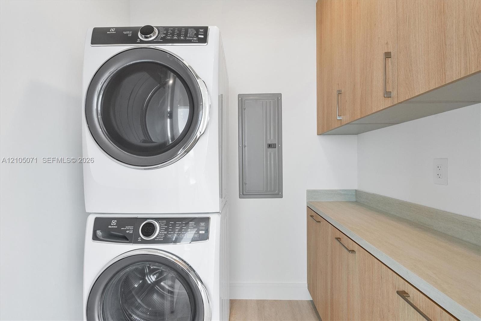 Stacked laundry center with built-in wood-finish cabinetry, countertop workspace, and metallic hardware