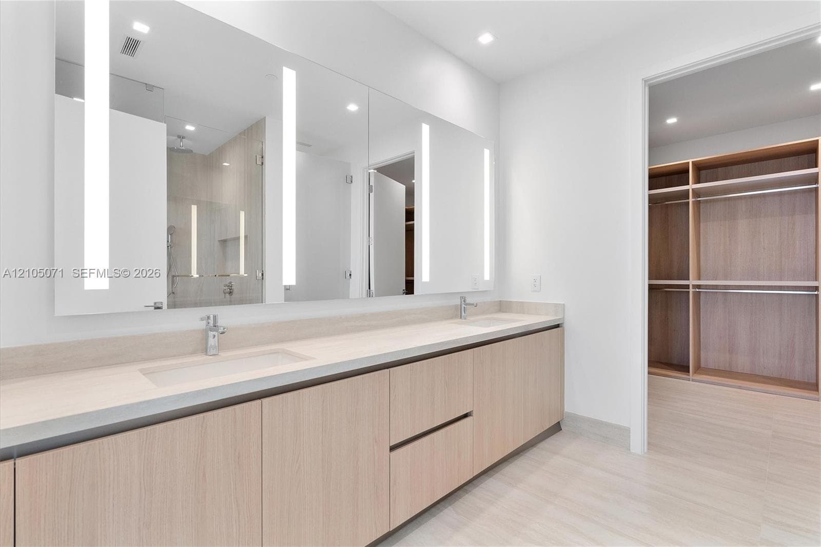 Dual-vanity cabinet with wood-finish cabinetry, solid-surface countertop, full-width mirror with integrated LED lighting, and custom walk-in closet featuring wood-finish shelving