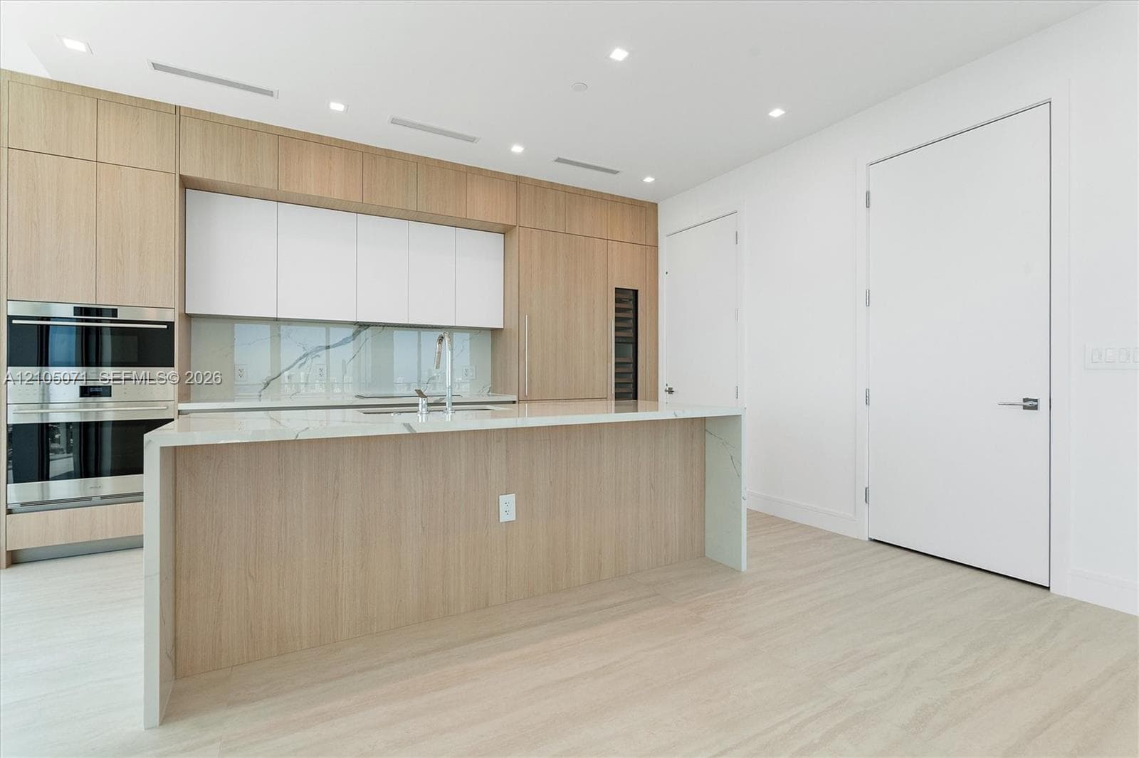 Kitchen featuring wood-finish cabinetry, waterfall-edge stone countertops, stainless steel wall ovens, a stone backsplash, and recessed lighting