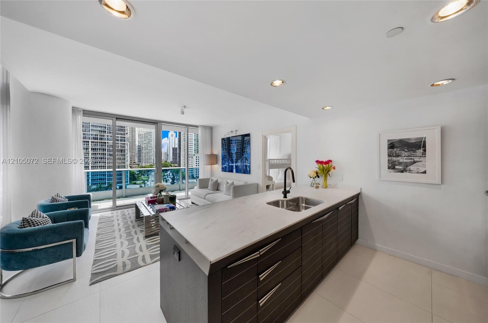 Contemporary kitchen with dark wood-grain cabinetry, Carrara marble island, and adjacent living area.