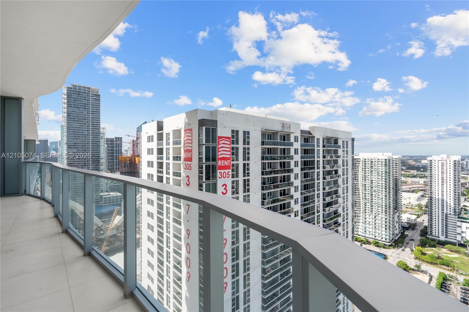 Private balcony featuring metal railings and a glass paneled enclosure overlooking an urban cityscape
