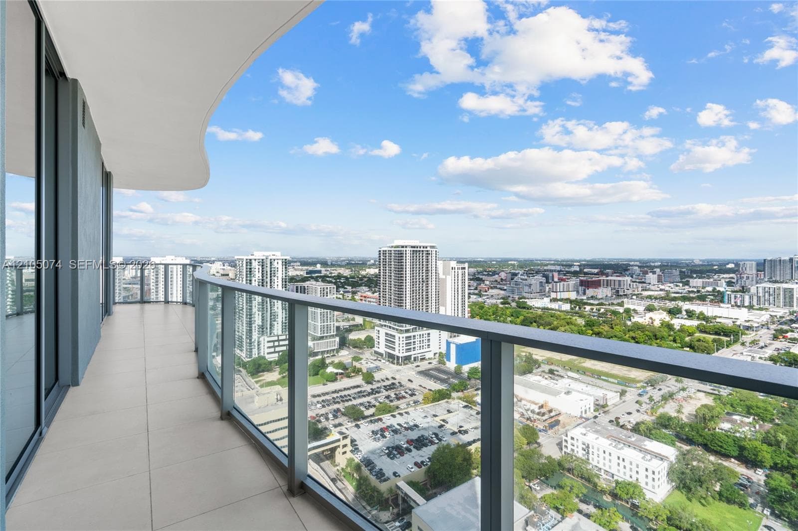 Spacious private balcony with large-format floor tiles and a curved structural design, featuring a glass-panel railing and extensive water and city skyline outlooks