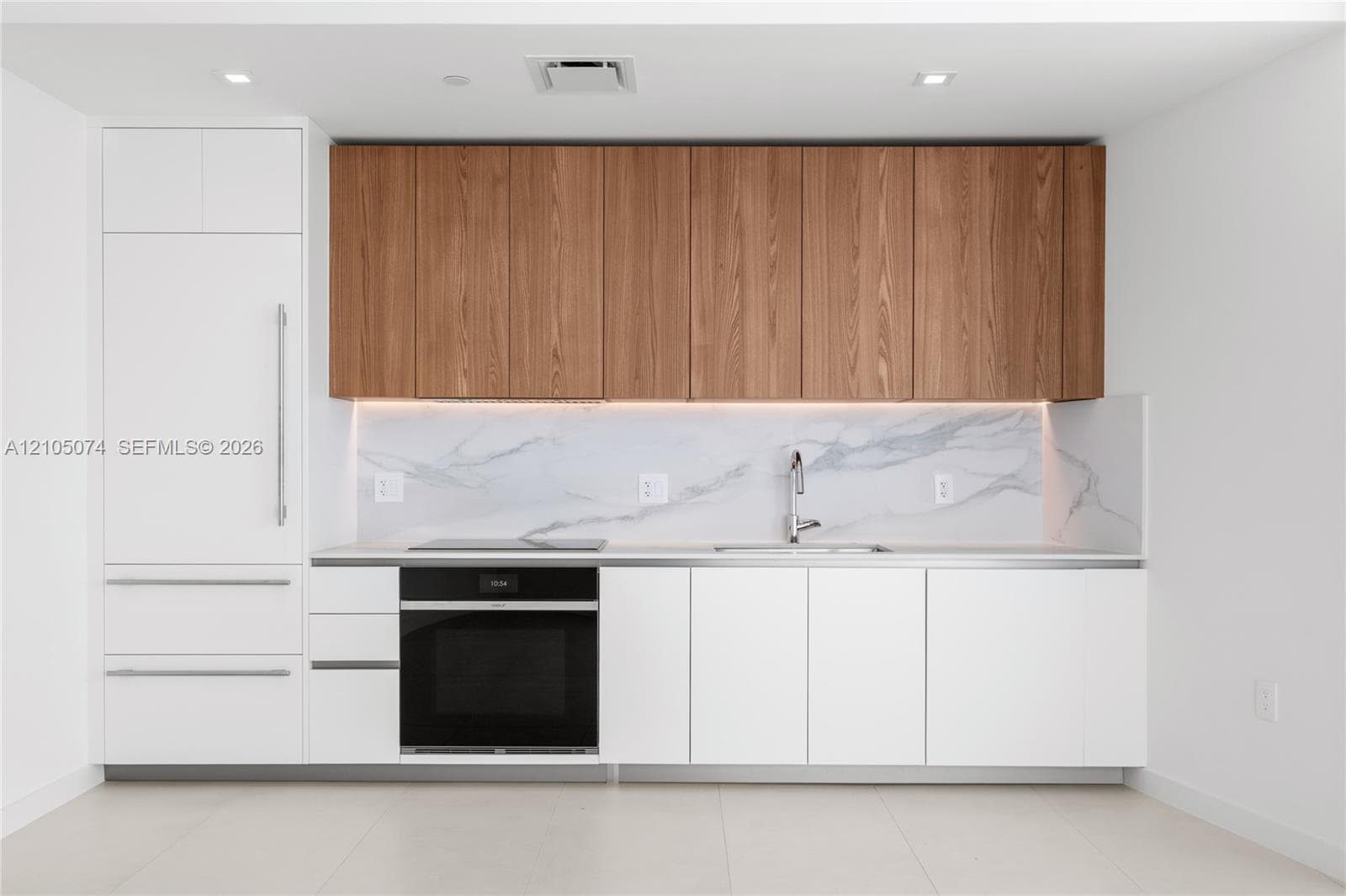 Modern kitchen featuring wood-finish upper cabinetry, matte white lower cabinetry, stone-patterned backsplash, integrated appliances, and floor-to-ceiling glass paneling