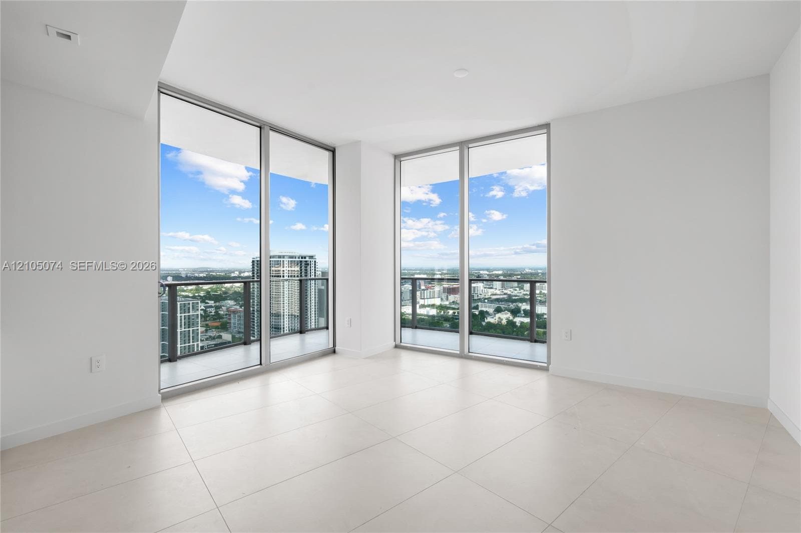 Floor-to-ceiling sliding glass doors, neutral tile flooring, and a glass-paneled balcony featuring urban skyline scenery