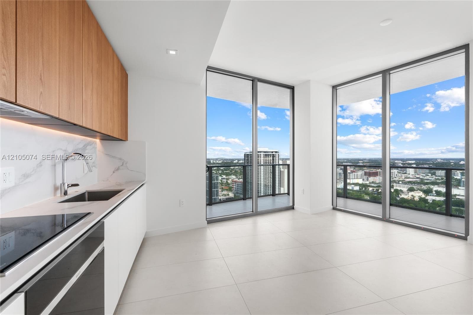 Floor-to-ceiling windows, private balcony with metal railing, sliding closet doors, wood-finish vanity with countertop basin, and stone-finish flooring