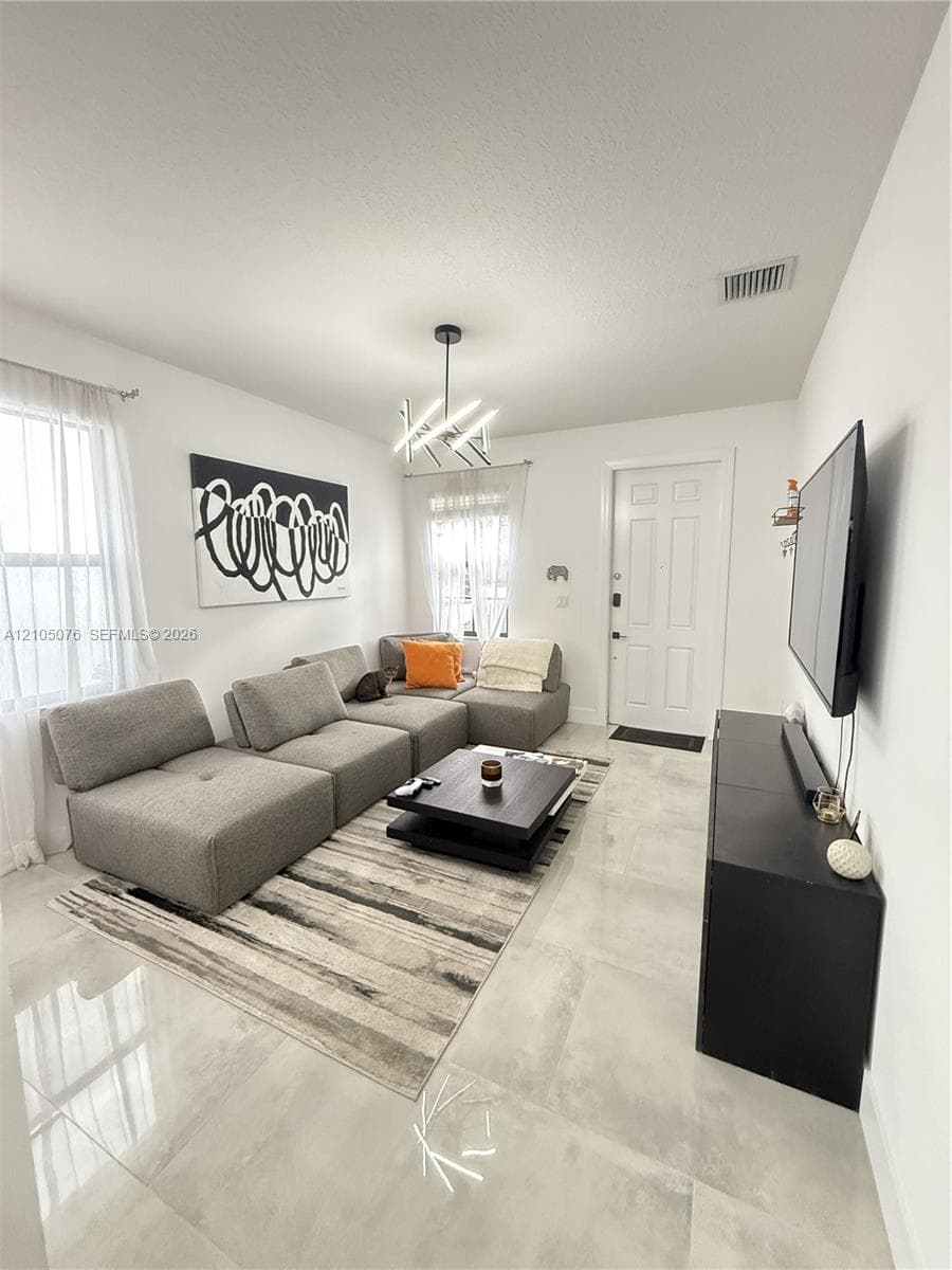 Living area featuring large-format light-toned tile flooring, multi-paned windows, and a contemporary geometric chandelier