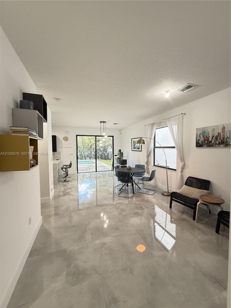 Open-concept interior featuring large-format tile flooring, recessed lighting, built-in wall shelving, and sliding glass doors revealing a swimming pool