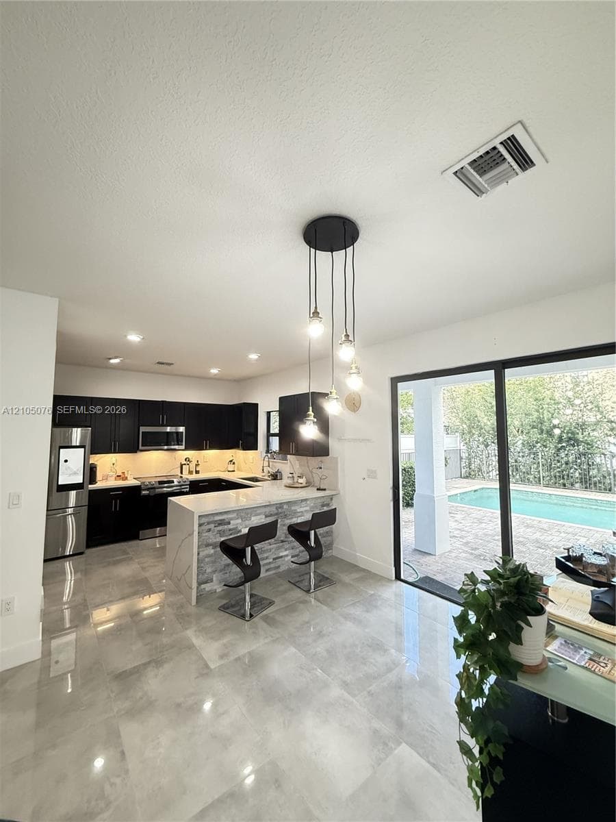 Kitchen featuring dark cabinetry, stone-finish countertops, stainless steel appliances, a stacked-stone kitchen island, and polished tile flooring