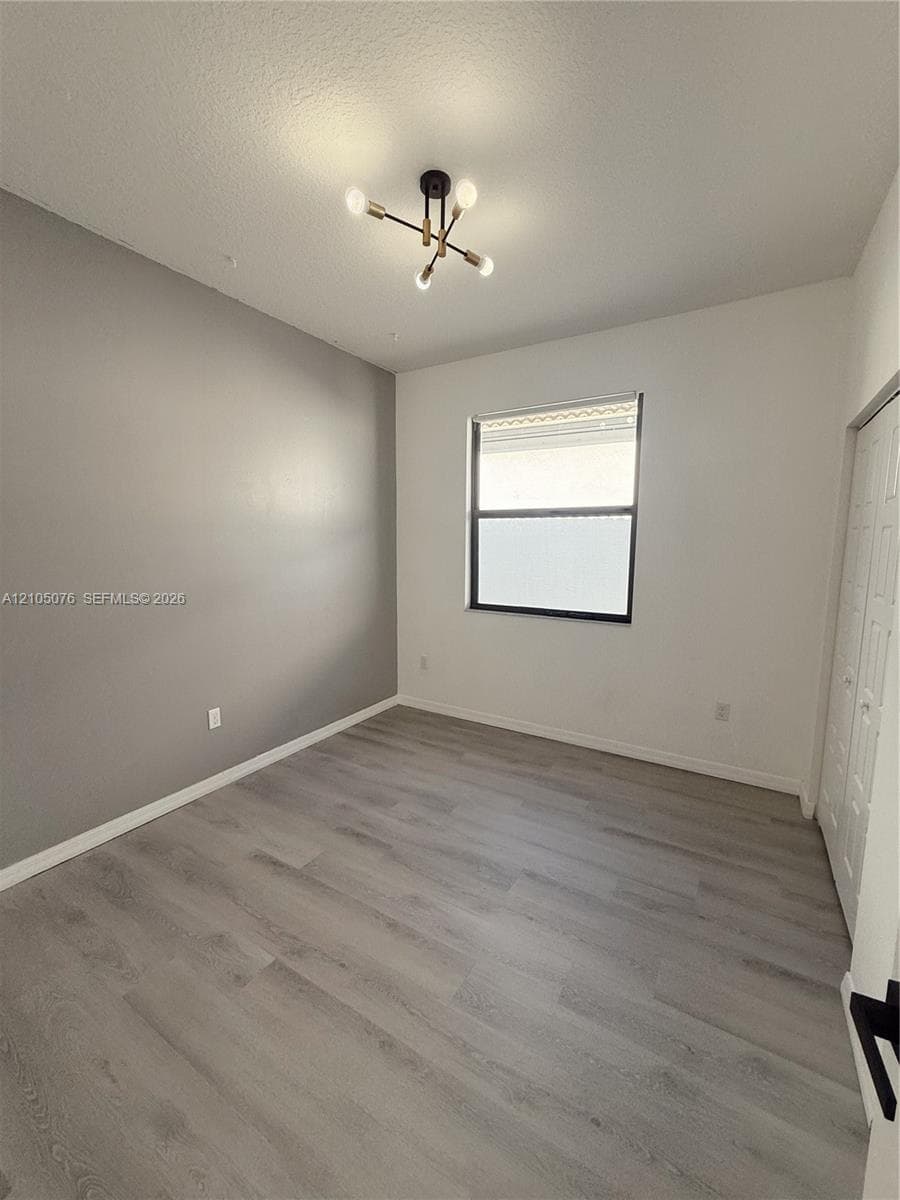 Interior room featuring wood-finish flooring, a multi-arm modern light fixture, a single window, and dual-panel closet doors