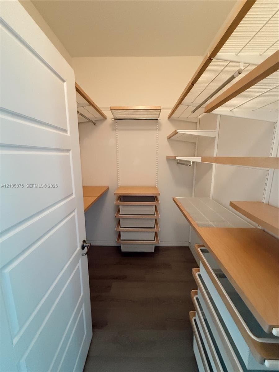 Walk-in closet featuring multi-level wood-finish shelving, integrated pull-out drawers, white metal support tracks, and dark wood-finish flooring