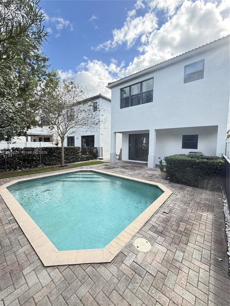 Private backyard featuring an in-ground swimming pool with a paved deck, multi-story stucco exterior, and black-trimmed windows