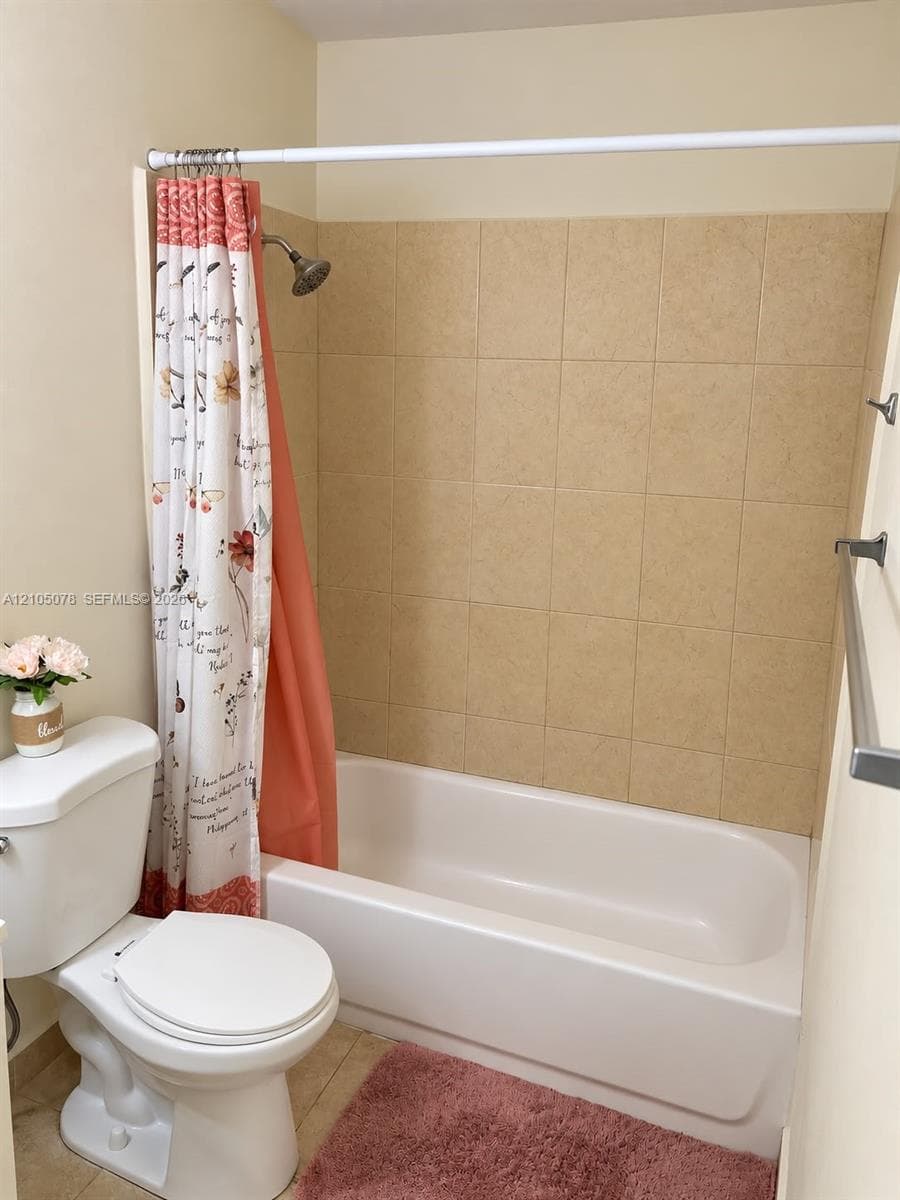 Full bathroom featuring a white porcelain toilet, a standard bathtub with an integrated surround, light-toned wall tile, and a brushed metal towel bar