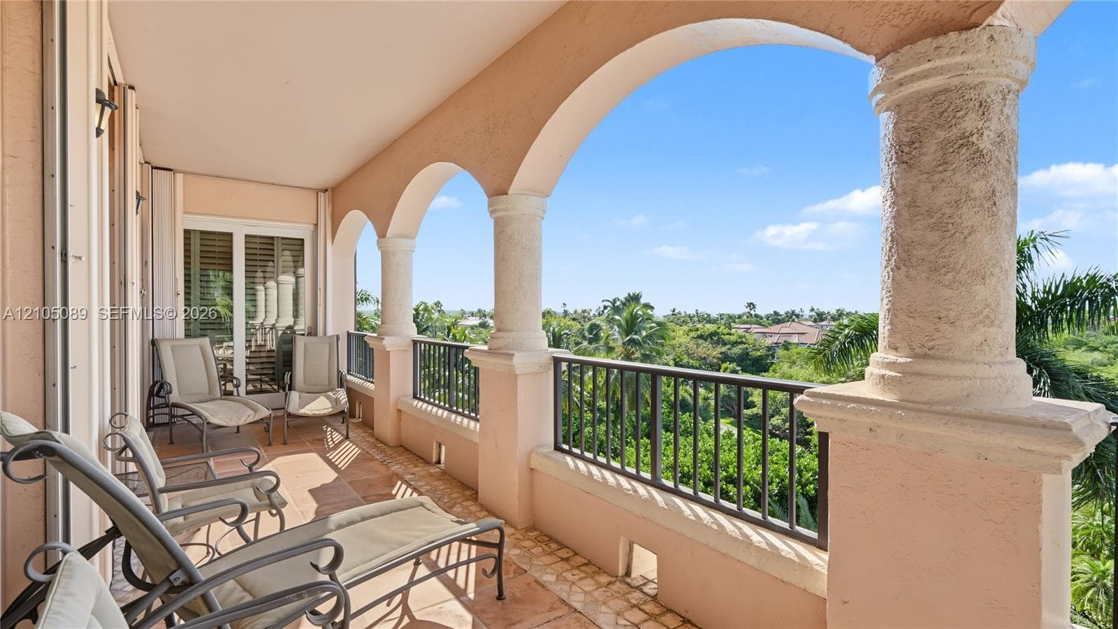 Covered balcony featuring arched architectural openings, stone-finish columns, metal railings, and tile flooring