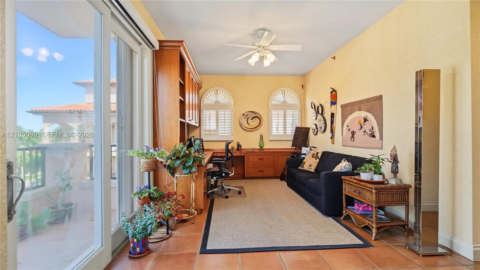Custom wood-finish built-in cabinetry, arched windows with plantation shutters, large-format terracotta tile flooring, sliding glass door, and a ceiling fan with integrated lighting