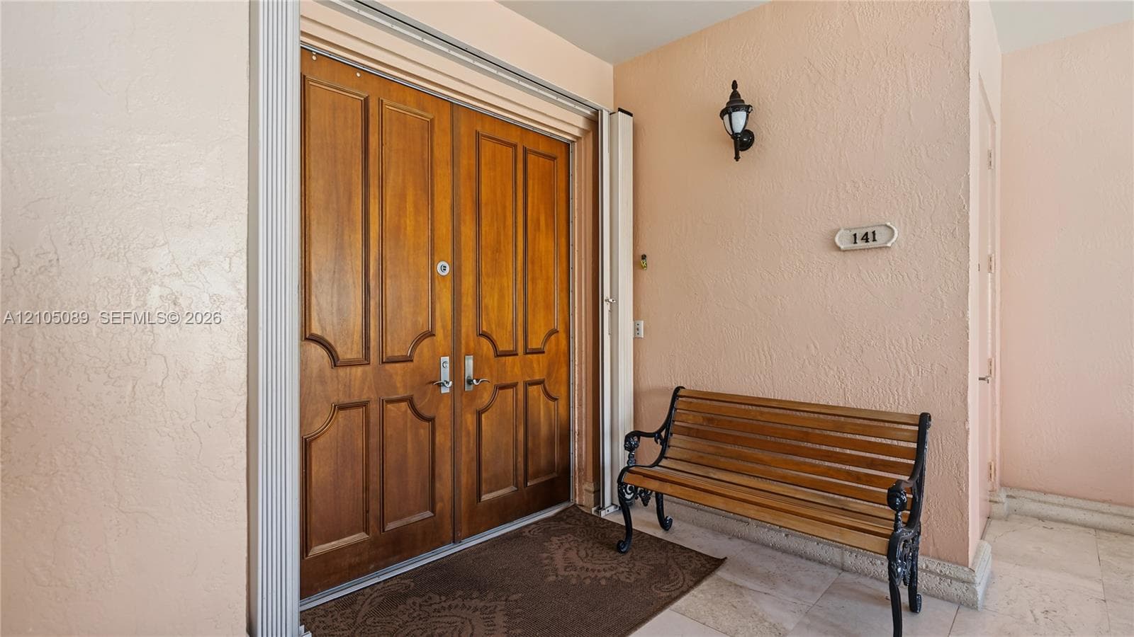Double entry doors featuring custom woodwork, paneled detailing, and metallic hardware, paired with textured wall finishes and stone-finish flooring