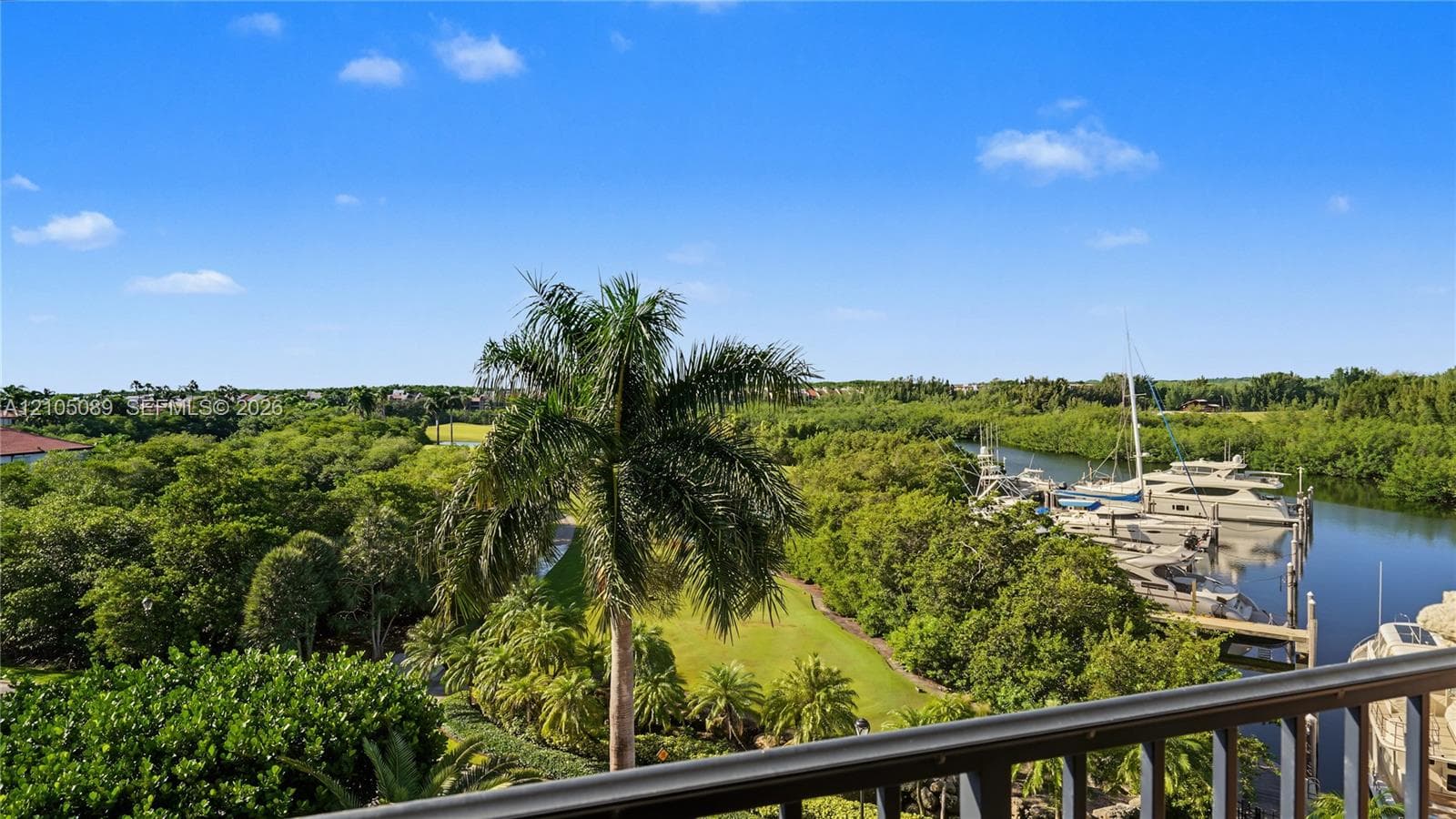 Elevated balcony featuring metal railings overlooking a marina with boat slips, mature landscaping, and palm trees