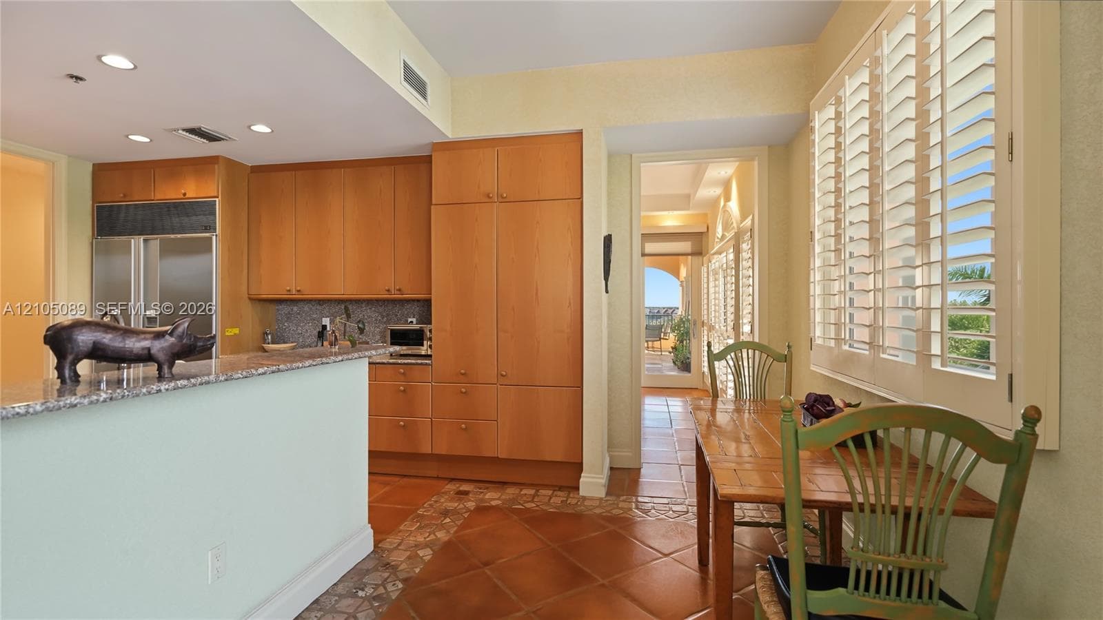Kitchen featuring wood cabinetry, stone countertops, tiled flooring, recessed lighting, and plantation shutters